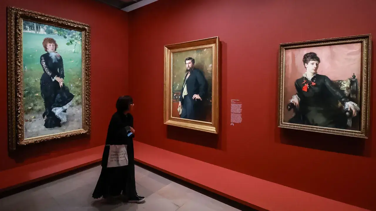 Une visiteuse admire des portraits lors d'une exposition &agrave; Paris. Les tableaux, aux cadres dor&eacute;s, sont accroch&eacute;s sur un mur rouge vif.