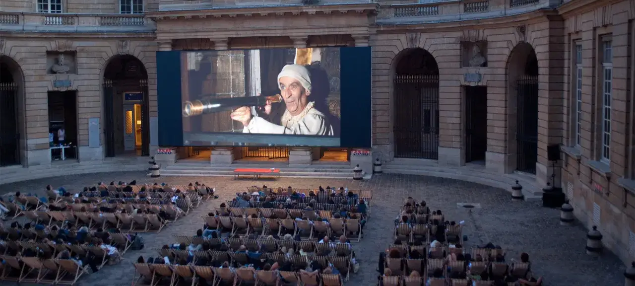 Un homme regarde dans une lunette sur un écran géant, lors d'une soirée cinéma plein air.