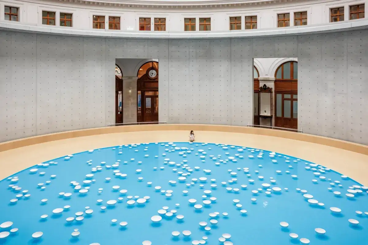 Une personne assise au bord d'une installation artistique bleue avec des disques blancs flottants &agrave; la Fondation Pinault Paris.