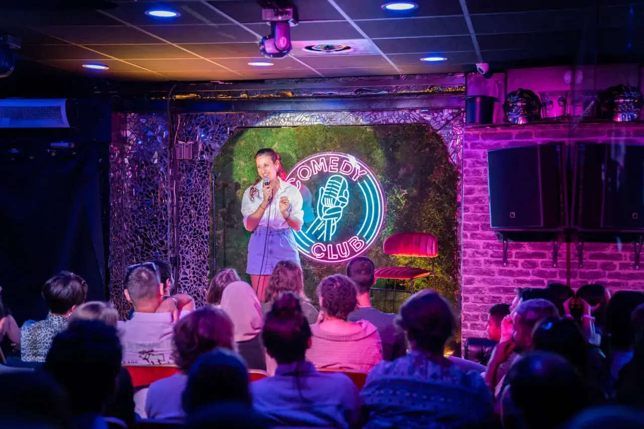 Une humoriste captive son public lors d'une soir&eacute;e de stand up comedy &agrave; Paris. L'ambiance est &eacute;lectrique sous les lumi&egrave;res n&eacute;on du club.