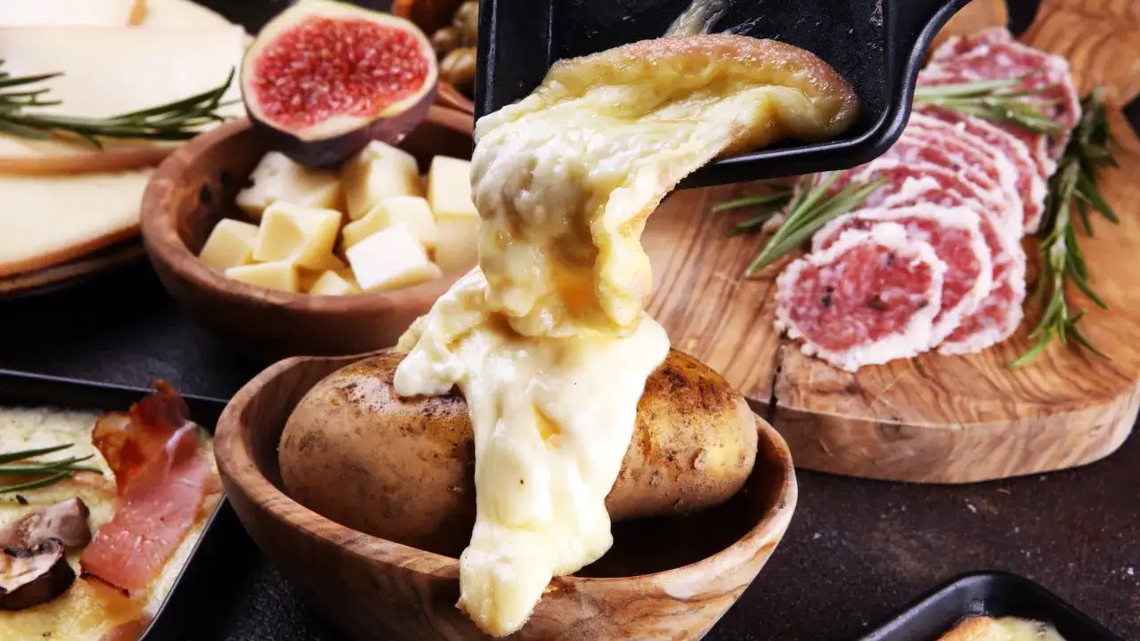 Un d&eacute;lice de raclette fondue sur une pomme de terre, accompagn&eacute; de charcuterie et de figues. Une exp&eacute;rience culinaire typique d'un restaurant raclette Paris.