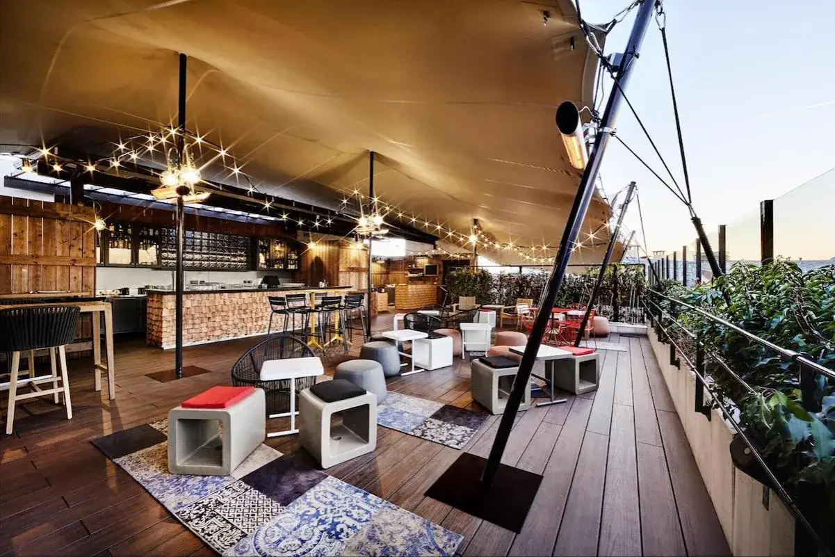 Ambiance chaleureuse sur un rooftop Paris pas cher, avec bar en bois, lumi&egrave;res festives et si&egrave;ges confortables.