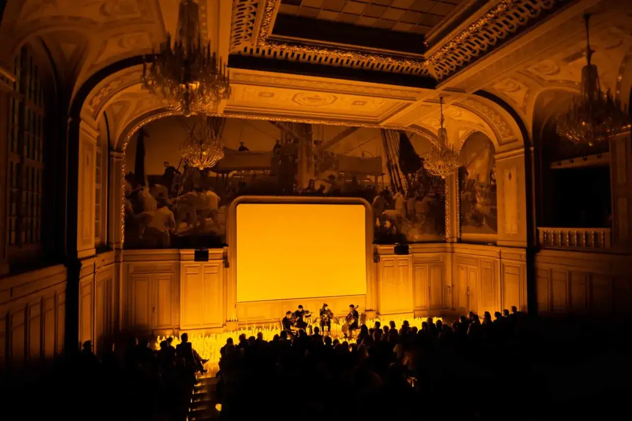 Concert intime &agrave; Paris, &eacute;clair&eacute; par la douce lueur de la candlelight. L'orchestre joue devant un &eacute;cran jaune, dans une salle orn&eacute;e de fresques et de lustres.