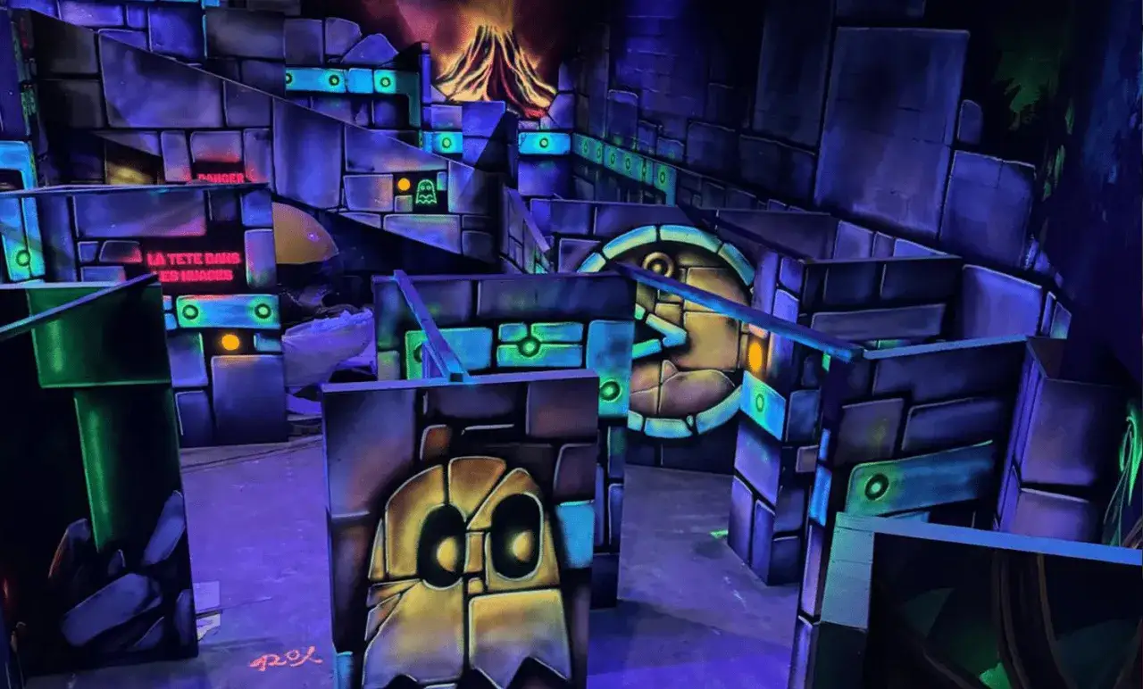 Labyrinthe de laser game aux couleurs vives, avec des murs en blocs, des fantômes et un volcan en arrière-plan. Le panneau