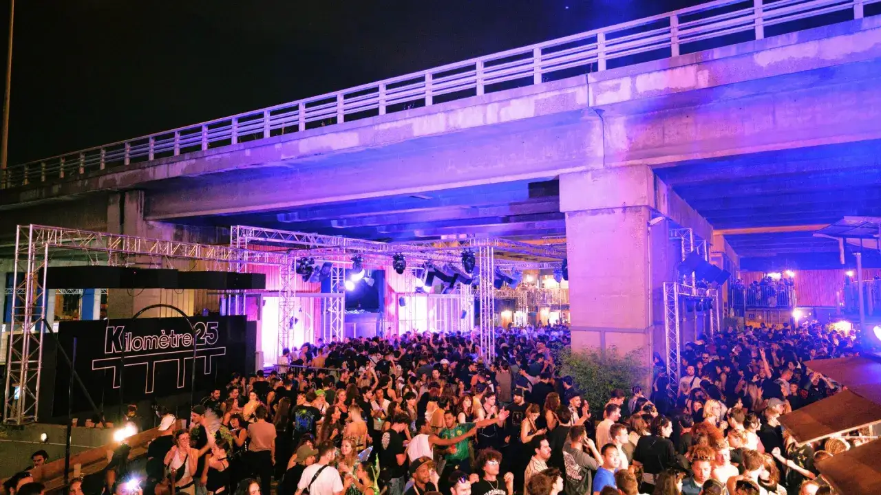 Foule en d&eacute;lire sous un pont illumin&eacute; de violet, devant un panneau 