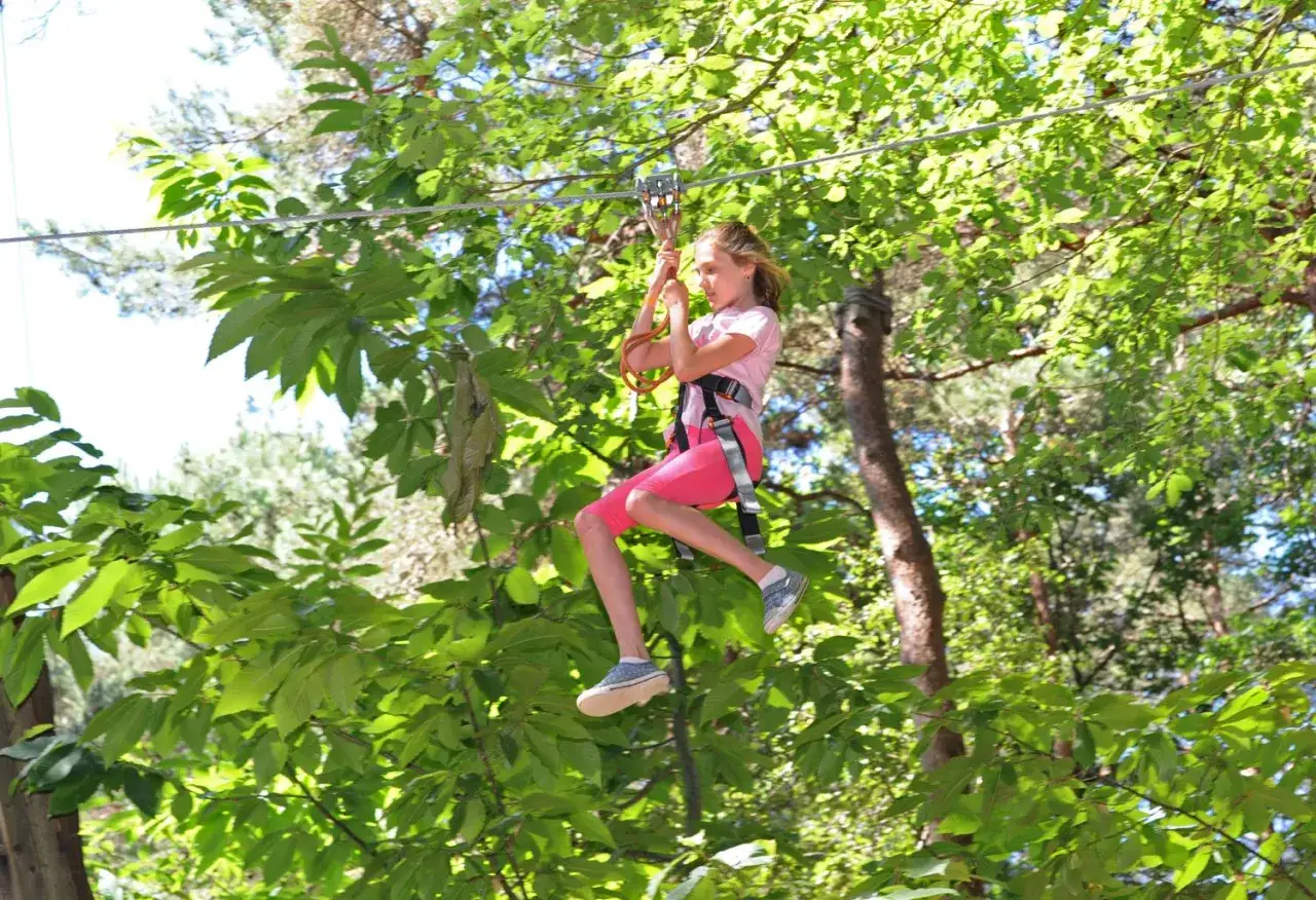 Une jeune fille profite d'une descente en tyrolienne lors d'une activit&eacute; d'accrobranche &agrave; Paris, entour&eacute;e de verdure luxuriante.