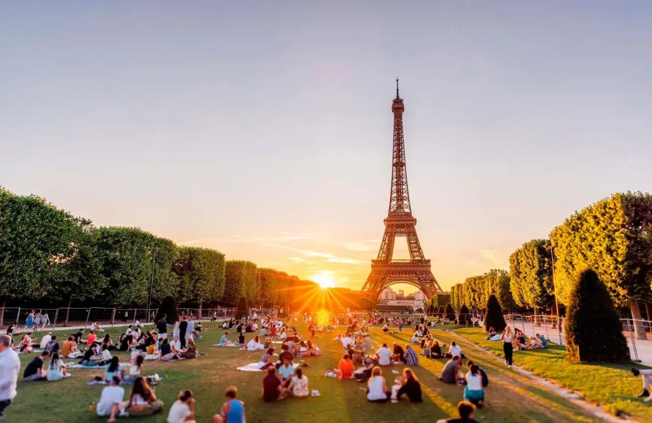 Un coucher de soleil dor&eacute; sur le Champ de Mars, id&eacute;al pour savoir que faire &agrave; Paris ce week-end. Des gens pique-niquent paisiblement.