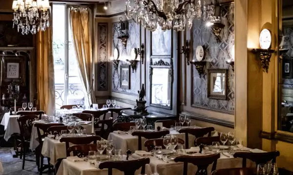 Tables dressées dans le plus vieux restaurant de Paris. Lustres en cristal, papier peint orné et vue sur la rue.