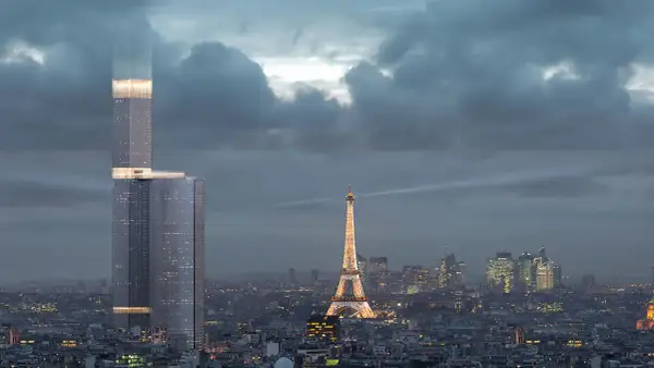 La Tour Montparnasse, en pleine rénovation, se dresse fièrement à Paris, illuminée par des faisceaux de lumière, dominant la ville et la Tour Eiffel scintillante.