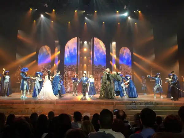 Scène du spectacle "Notre-Dame de Paris" avec des costumes d'époque et un décor évoquant la ville.