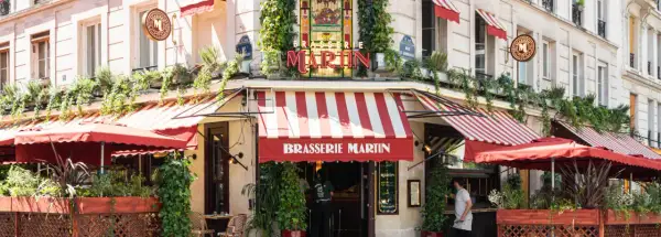 La Brasserie Martin, un coin parisien charmant avec ses auvents rayés rouges et blancs, ses plantes grimpantes et son enseigne lumineuse.