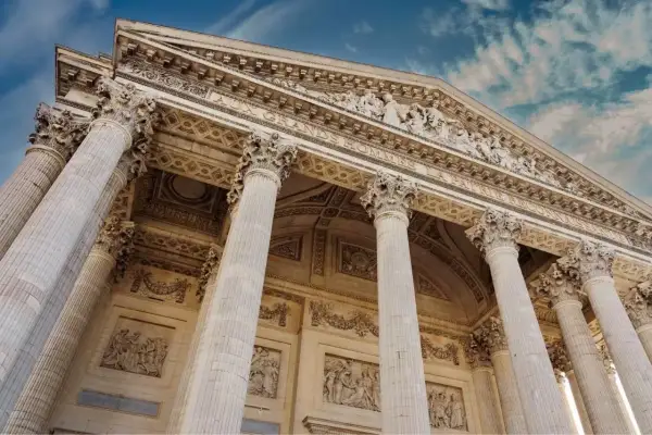 Le **Panthéon de Paris**, majestueux avec ses colonnes imposantes et ses bas-reliefs, se dresse sous un ciel bleu nuageux.