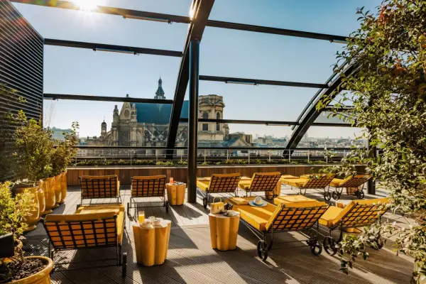 Profitez d'un brunch rooftop à Paris avec vue sur les toits et une église majestueuse. Des chaises longues jaunes invitent à la détente.