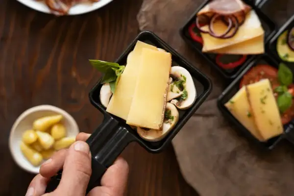 Poignée de raclette avec fromage, champignons et basilic, prêt pour un dîner dans un restaurant raclette Paris.