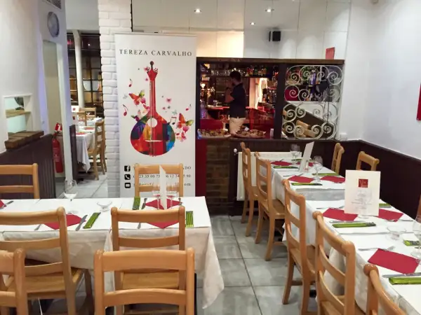 Tables dressées dans un restaurant portugais. Un homme derrière le bar, une guitare colorée sur une bannière.
