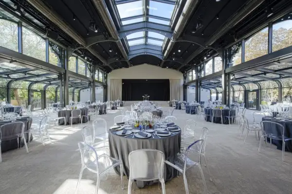 Salle de réception lumineuse au pavillon Gabriel, tables rondes dressées sous une verrière, chaises transparentes.