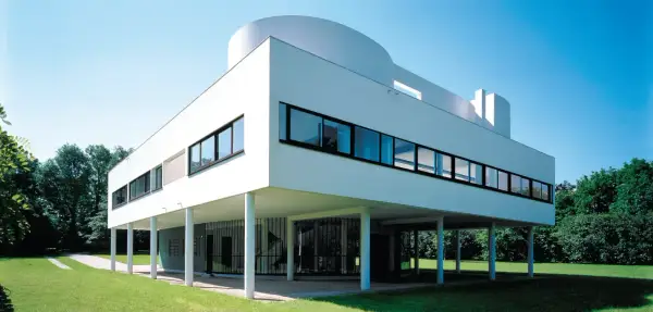 La Villa Savoye, icône de l'architecture moderne, se dresse sur pilotis dans un écrin de verdure, sous un ciel bleu éclatant.