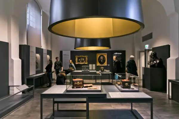 Visiteurs admirant des objets d'art et des portraits dans une exposition au musée Monnaie de Paris.