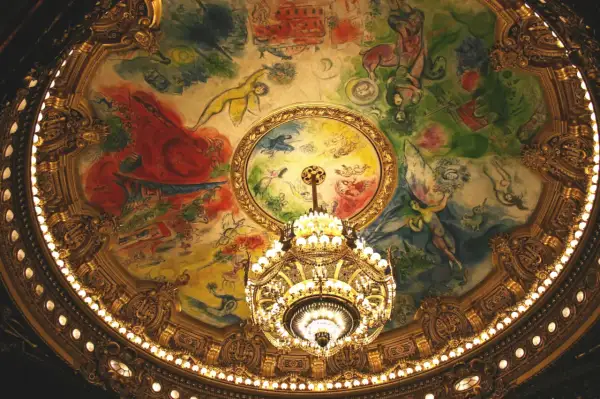 Le plafond peint de la **place de l'Opéra** est illuminé par un lustre doré. Des figures célestes dansent sur une toile colorée.