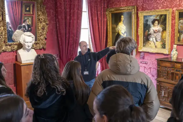 Visite guidée dans la Maison de Victor Hugo à Paris. Un guide montre des tableaux et un buste de l'écrivain à un groupe de visiteurs.