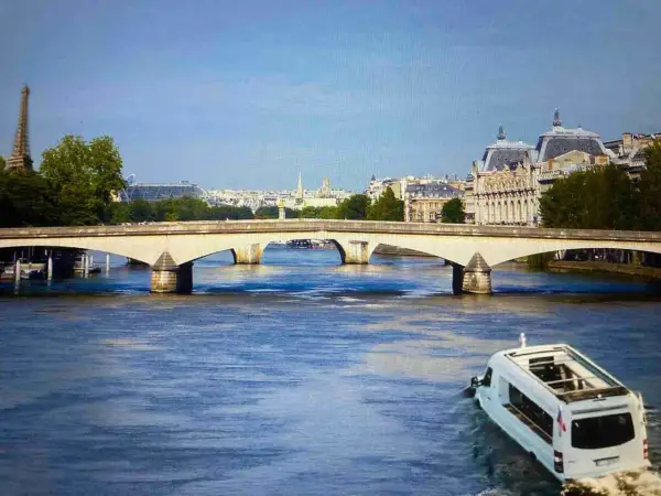 Un bus amphibie navigue sur la Seine, sous un pont parisien, avec la Tour Eiffel et des bâtiments emblématiques en arrière-plan. On dirait que même les canards de Paris ont leur propre moyen de transport !