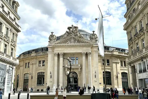 Le musée de la Bourse, un bâtiment majestueux, accueille des visiteurs sous un ciel nuageux. Une sculpture d'arbre intrigante se dresse devant l'entrée.