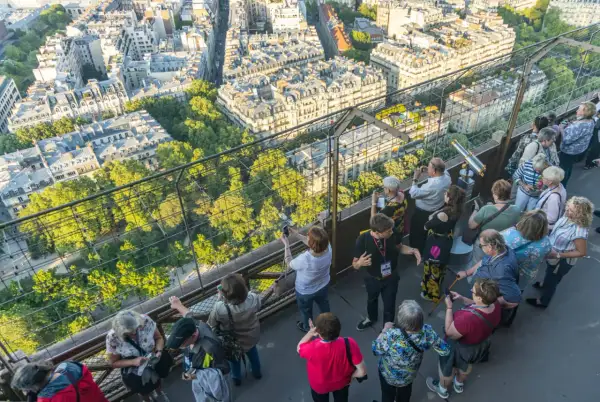 Vue panoramique de Paris depuis la Tour Eiffel, avec des touristes admirant le paysage. Le soleil d'été suggère le meilleur moment pour visiter la Tour Eiffel.