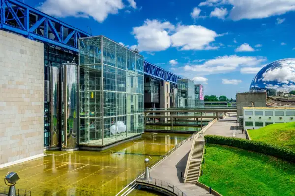 Le bâtiment moderne de la Cité des sciences Paris, avec ses structures en verre et en métal, reflète le ciel bleu et les nuages.
