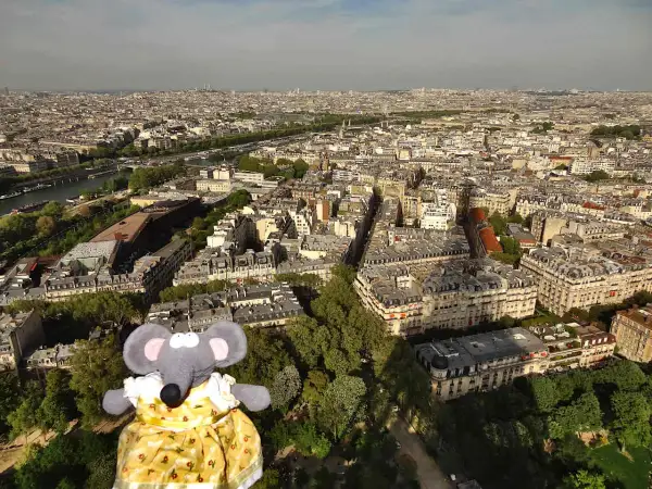 Une souris en robe jaune admire Paris depuis le sommet de la Tour Eiffel.