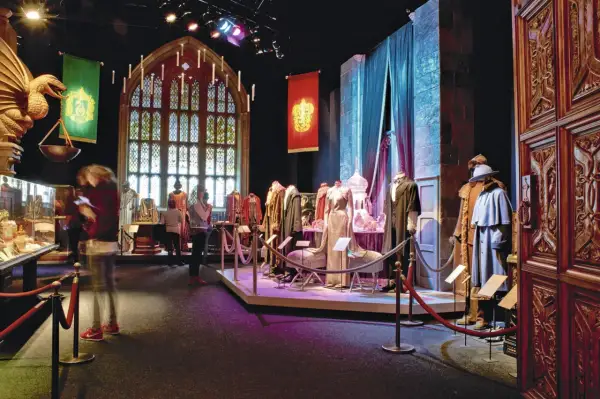 Costumes et artefacts de l'exposition Harry Potter, avec des bannières de Poudlard et une grande fenêtre gothique.