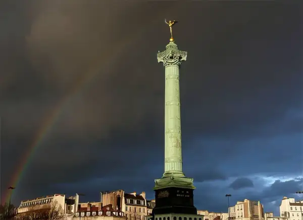 La colonne de Juillet se dresse fièrement sur la place de la Bastille, sous un ciel orageux traversé par un arc-en-ciel.