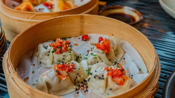 Délicieux dim sum à Paris, servis dans un panier en bambou, garnis de garnitures vibrantes et de graines de sésame.