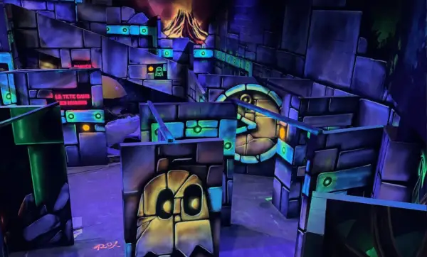 Labyrinthe de laser game aux couleurs vives, avec des fantômes et un volcan en arrière-plan. Le panneau "LA TÊTE DANS LES NUAGES" suggère une expérience amusante.