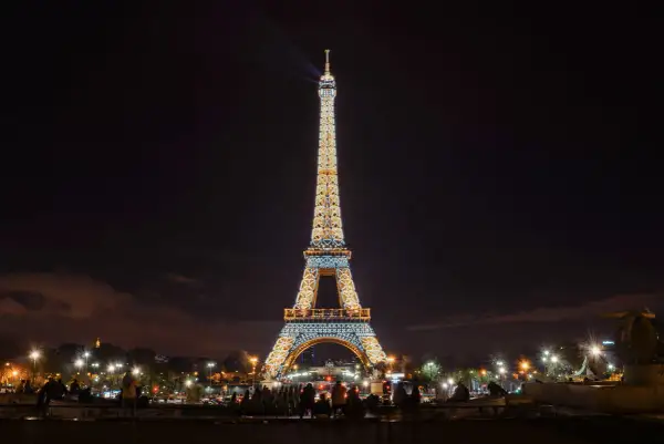 La Tour Eiffel illuminée la nuit, un spectacle magique avec des faisceaux de lumière traversant le ciel parisien.