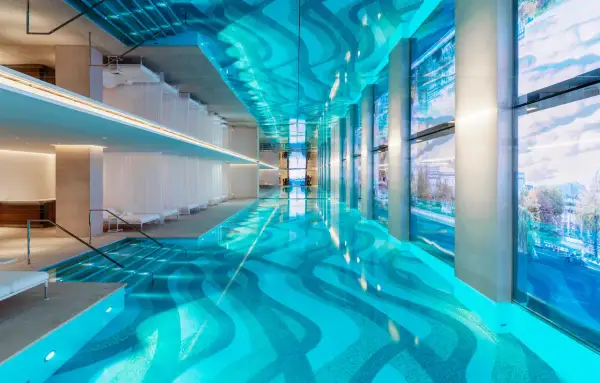 Piscine intérieure luxueuse d'un spa à Paris, avec un éclairage bleu vif, des voilages blancs et une vue sur la ville.
