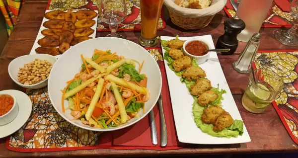 Un festin dans un restaurant antillais : salade de crevettes, accras, bananes plantain frites et un cocktail rafraîchissant.