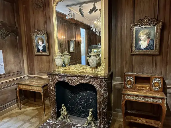 Un salon d'époque avec des portraits d'enfants, une cheminée en marbre et des meubles anciens. On imagine le cognacq jay dégusté dans ce cadre.