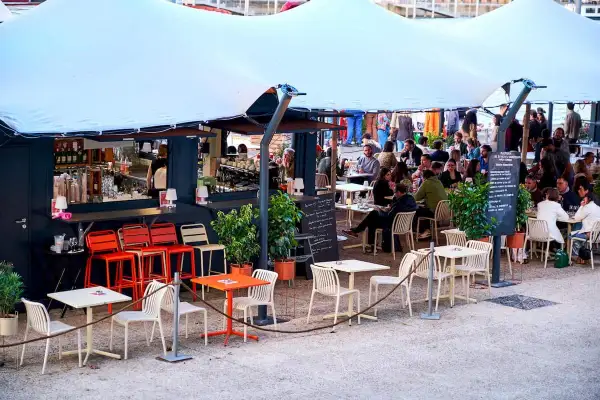 Bar animé sur les quais parisiens, avec des tables et des chaises en terrasse sous une grande tente blanche.