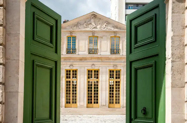 Portes vertes ouvertes sur le pavillon Vendôme à Paris, avec sa façade ornée et ses grandes fenêtres jaunes.