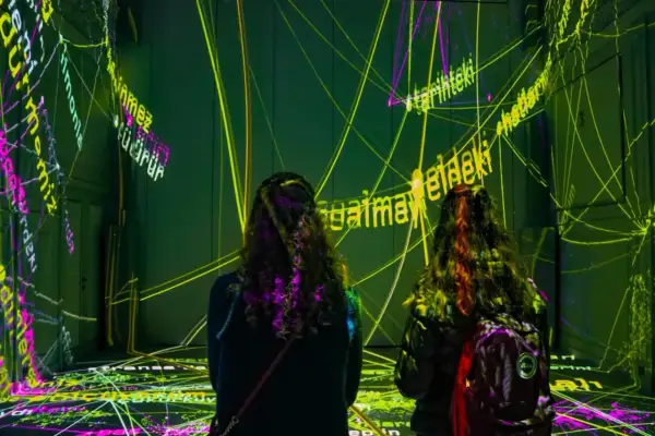 Deux personnes découvrent une exposition immersive à Paris, baignée de lumières vives et de textes projetés.