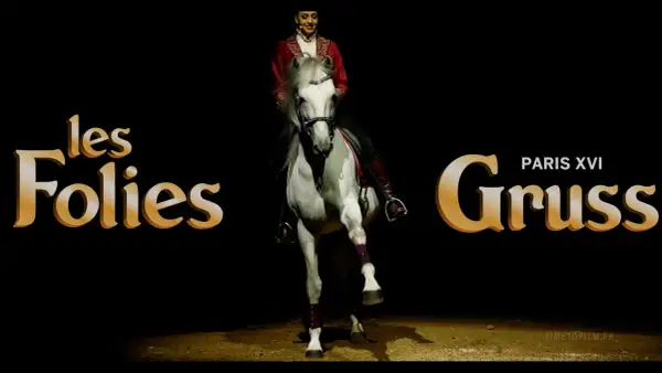 Une écuyère en tenue rouge sublime un cheval blanc lors d'un spectacle des Folies Gruss.